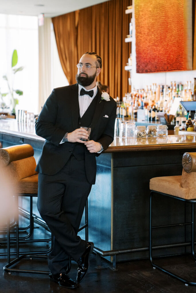 Groom standing at hotel bar in black tuxedo, Tampa destination wedding photography