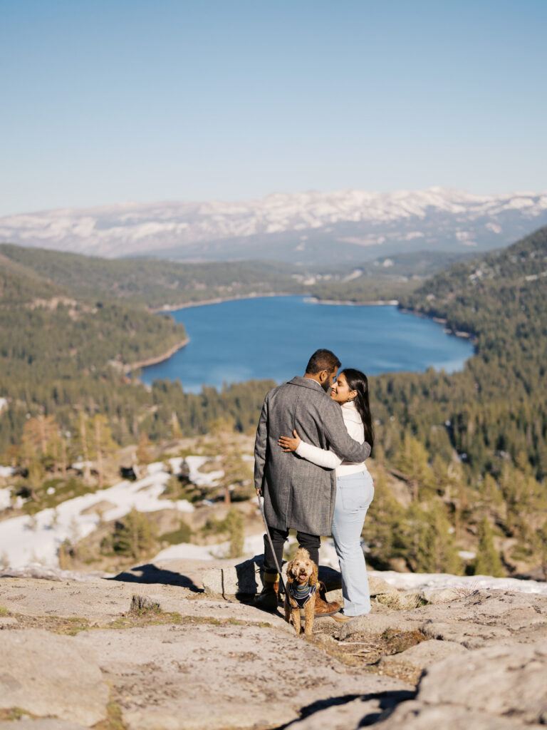 Couple loooking into each other eyes at donner lake overlook, dog looking at the camera, the background shows all donner lake