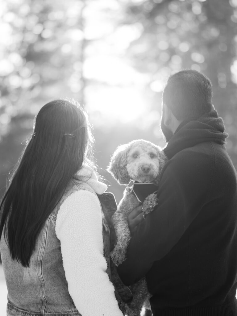Couple in their backs while dog is in the center looking at the camera, photo is black and white