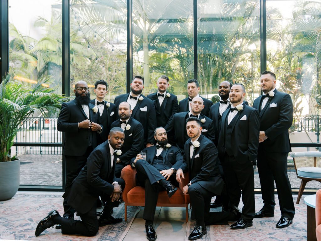 Groom and groomsmen in black tuxedos posed inside modern hotel with tropical views, Tampa wedding photography