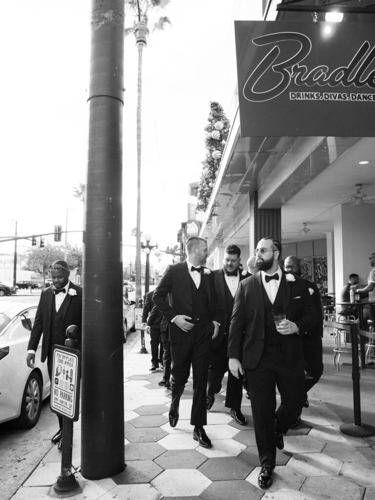 Groom and groomsmen in black tuxedos on Ybor City sidewalk, black and white wedding portrait Tampa