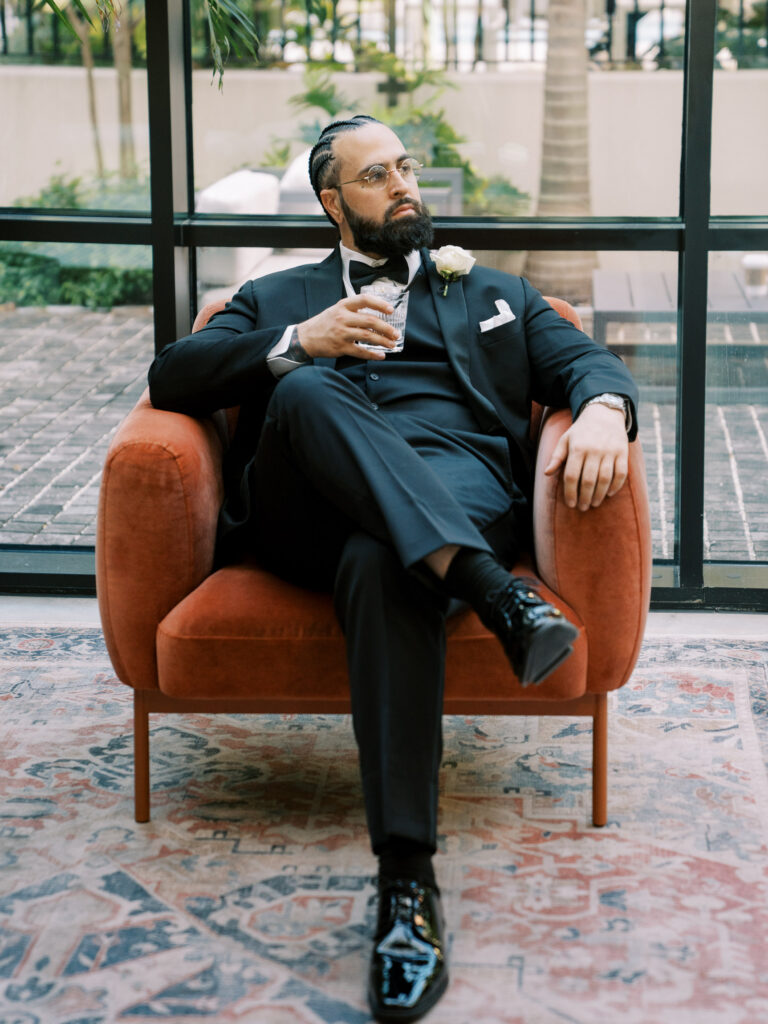 Groom in black tuxedo seated in velvet chair, fine art wedding portrait Ybor City Tampa