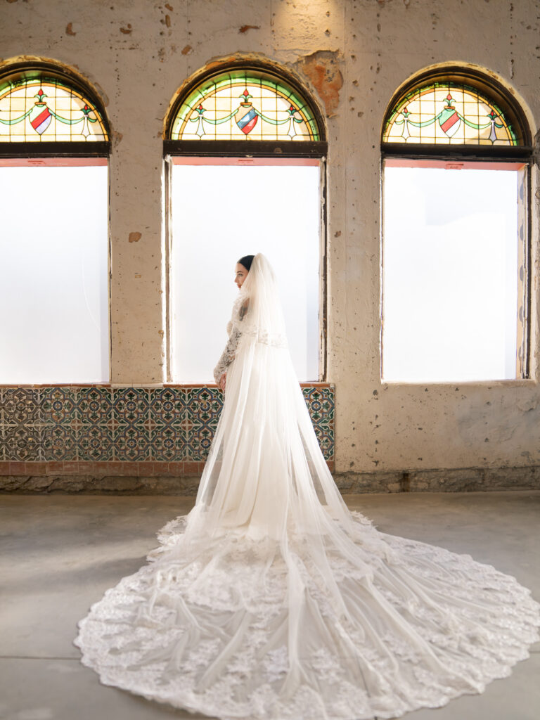 Bride in cathedral lace veil and off-shoulder gown standing before stained glass windows, Ybor City wedding venue
