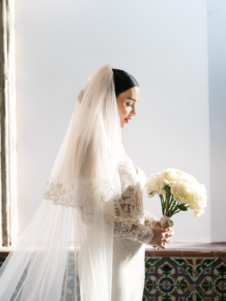 Bride holding white peony bouquet beneath cathedral veil against stained glass, fine art bridal portrait Tampa