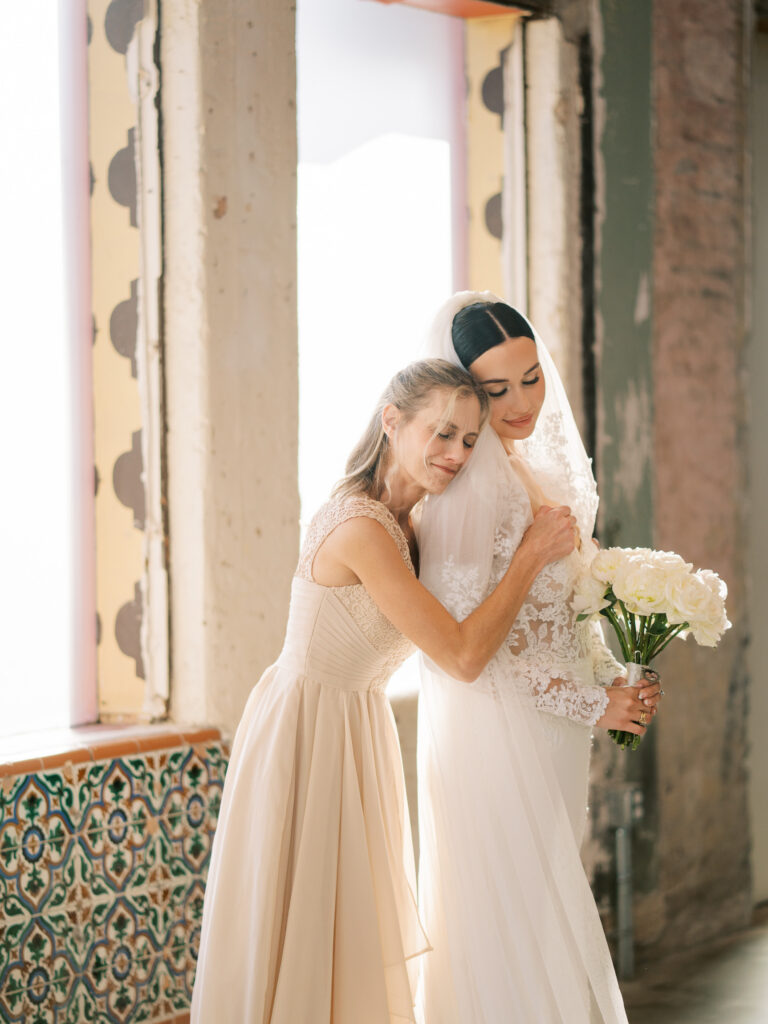 Bride and mother embracing near arched windows with hand-painted tile walls, Tampa wedding photography