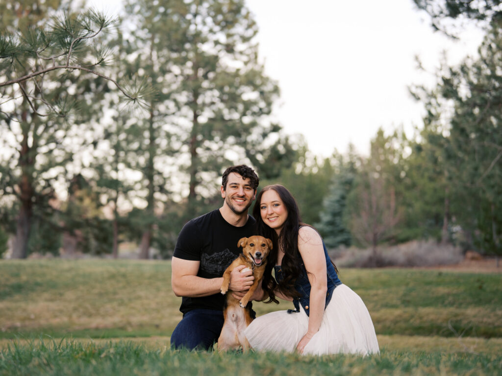 Couple smiling at the camera with their dog at golden hour captured by a Reno photographer in a couples session