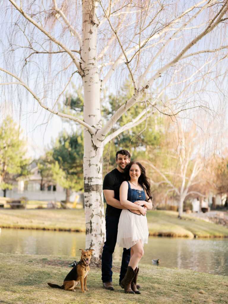 Couple smiling at the camera with their dog by their side who also smiles at the camera captured by a Reno photographer in a couples session