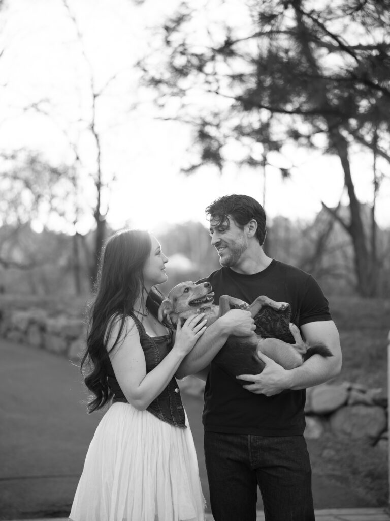 Black and white photo of couple holding their dog like a baby and smiling at each other captured by a Reno photographer in a couples session
